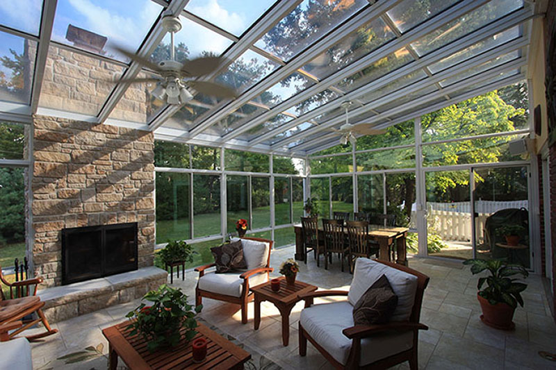 Interior of a sunroom with a dining room table, outdoor chairs and a coffee table, and a fireplace with a ceiling fan overhead.