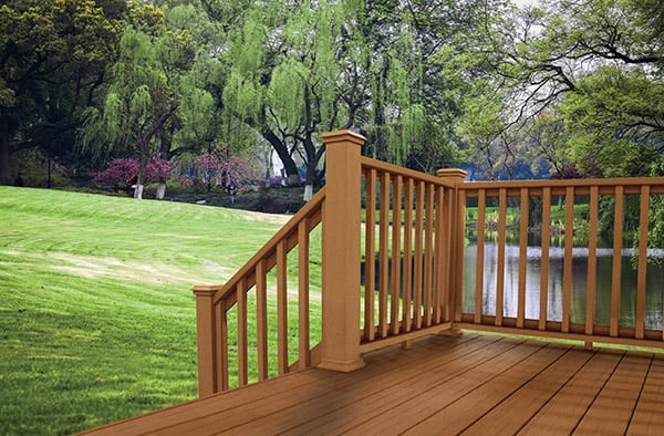 The corner of a deck with a railing bordering it and steps leading down to a large lawn with trees and a lake in the background.   